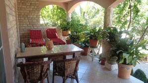 A covered patio with a table and chairs, surrounded by potted plants and a stone wall. - Apartment in Biograd na Moru with Terrace, Air condition, WIFI, Dishwasher (4818-7) (Biograd na moru)