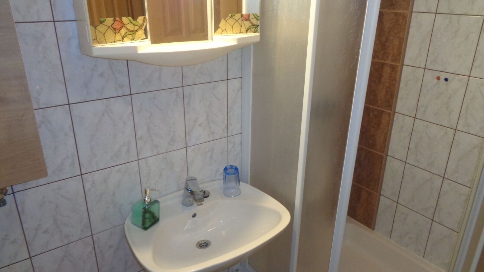 A bathroom with a sink, a mirror, and a shower area.