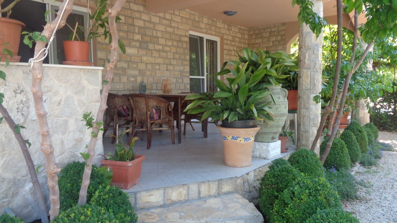 A stone building with a covered porch, potted plants, and a table with chairs.