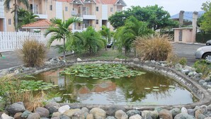 A pond with rocks and plants, surrounded by a white fence and palm trees.