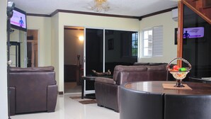 A living room with a brown leather sofa, a round coffee table, and a TV mounted on the wall.