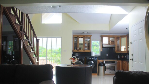 A spacious living area with a staircase, a round coffee table, and a kitchen in the background.