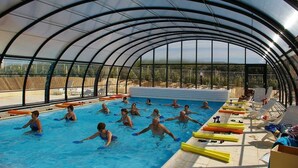 An indoor swimming pool with a curved glass ceiling, surrounded by lounge chairs and poolside amenities.