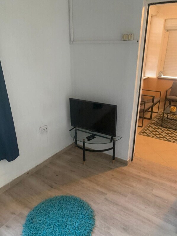 A room with a television on a stand, a blue rug, and a door leading to another room with a table and chairs.