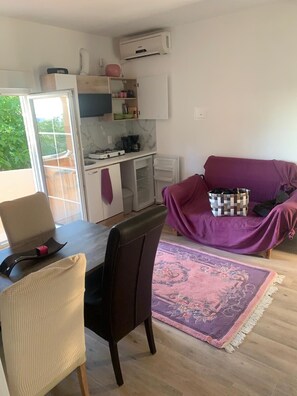 A compact living space with a dining area, a kitchenette, a purple sofa, and a view of greenery outside. - Apartment in Vrsi with Balcony, Air condition, WIFI (4824-5) (Vrsi)