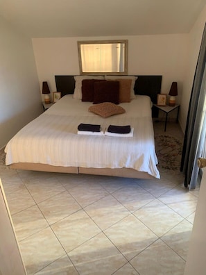 Un dormitorio con una cama grande, dos mesitas de noche, una ventana y una puerta.