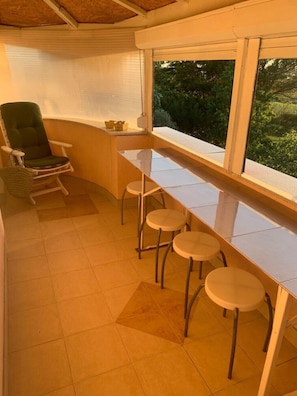 Habitación con barra, una butaca acolchada y ventana con vistas a vegetación.