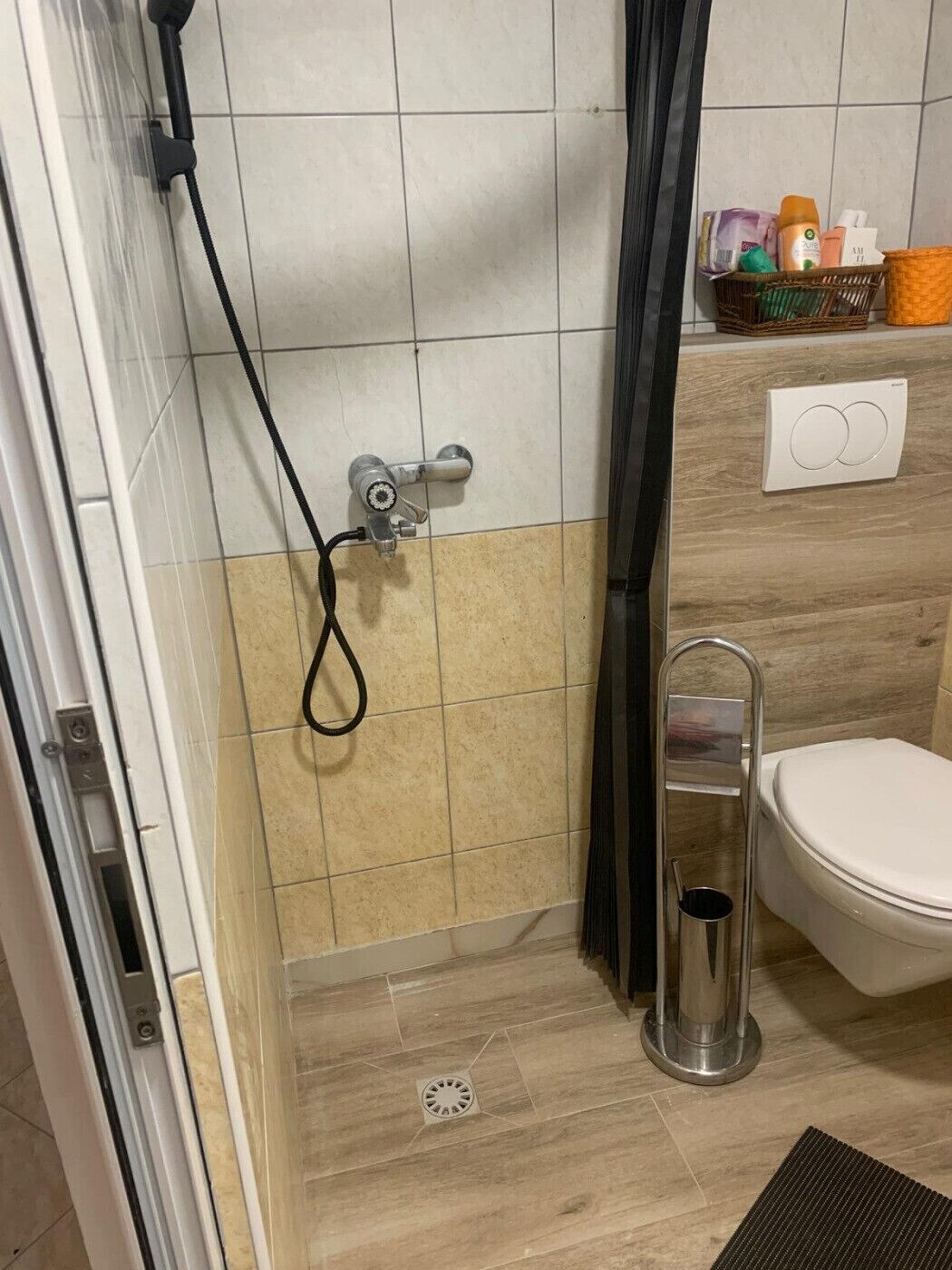 A bathroom with a shower, toilet, and a small shelf with toiletries.