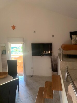 A modern living room with a TV, a sofa, a dining area with a table and chairs, and a view through an open door. - Apartment in Vrsi with Seaview, Terrace, Air condition, WIFI (4824-7) (Vrsi)