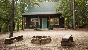 A rustic cabin with a fire pit in the center, surrounded by wooden benches.