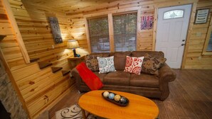 A cozy cabin interior with a brown leather sofa, a wooden coffee table, and a patterned rug.