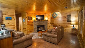 A cozy cabin interior with wooden walls, a fireplace, a sofa, and a small table.