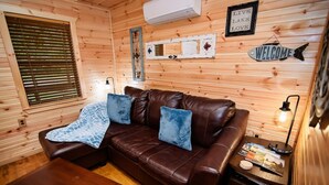 Een gezellig chaletinterieur met een bruine leren bank, een houten tafel en een klein bijzettafeltje met een lamp.