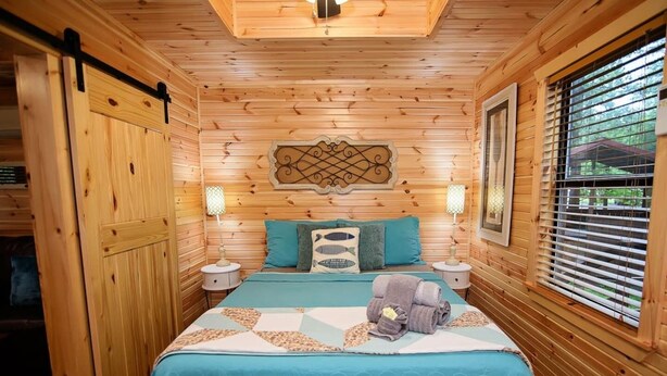 Een houten kamer met een bed, twee nachtkastjes, een decoratief object aan de muur en een raam met zonwering.