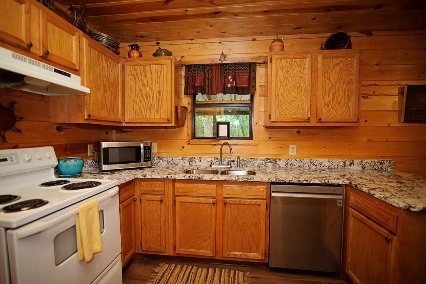 Une cuisine avec des meubles de rangement en bois, un four à micro-ondes, une cuisinière, un évier et un lave-vaisselle.