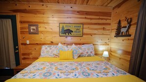 Une chambre rustique en bois avec un lit, une pancarte indiquant « Ne réveillez pas l’ours » et une image d’ours accrochée au mur.