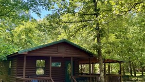 Une cabane en bois avec un porche, entourée d’arbres.