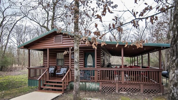Une cabane rustique dotée d’un porche, d’une terrasse couverte et d’un petit jardin devant.