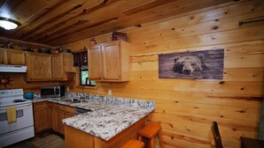 Une cuisine rustique, située dans un chalet en bois, avec des comptoirs en granit, des armoires en bois, un four à micro-ondes et un tableau représentant un chien.