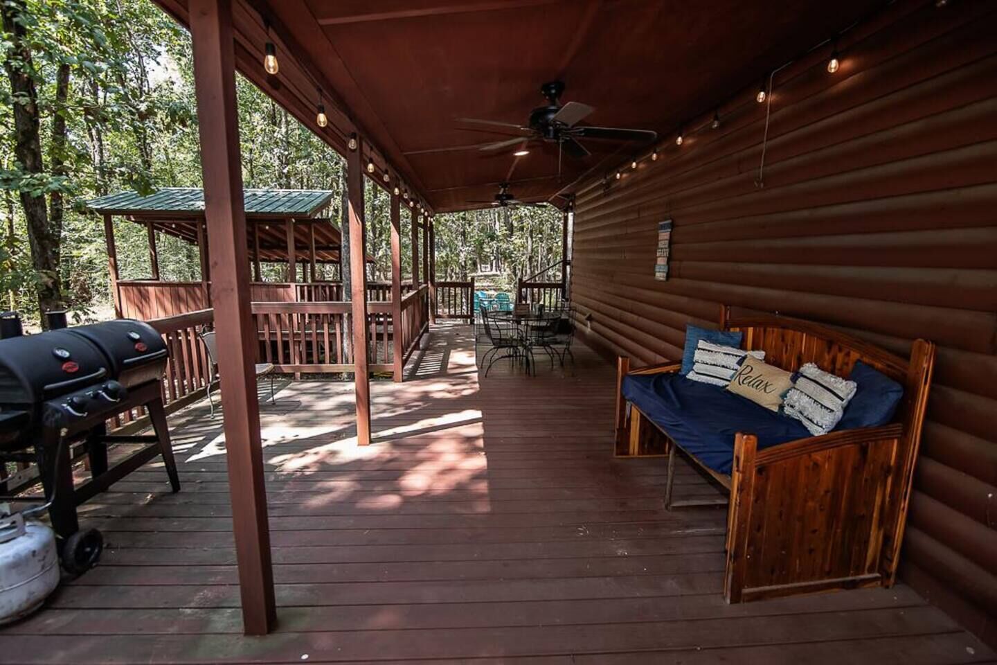 A covered porch with a wooden bench, a grill, and a ceiling fan.