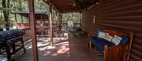A covered porch with a wooden bench, a grill, and a ceiling fan.