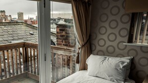 A balcony with a view of city buildings, a wooden railing, and a bed with a pillow. - Infinity Apartments Victoria Street (Liverpool)
