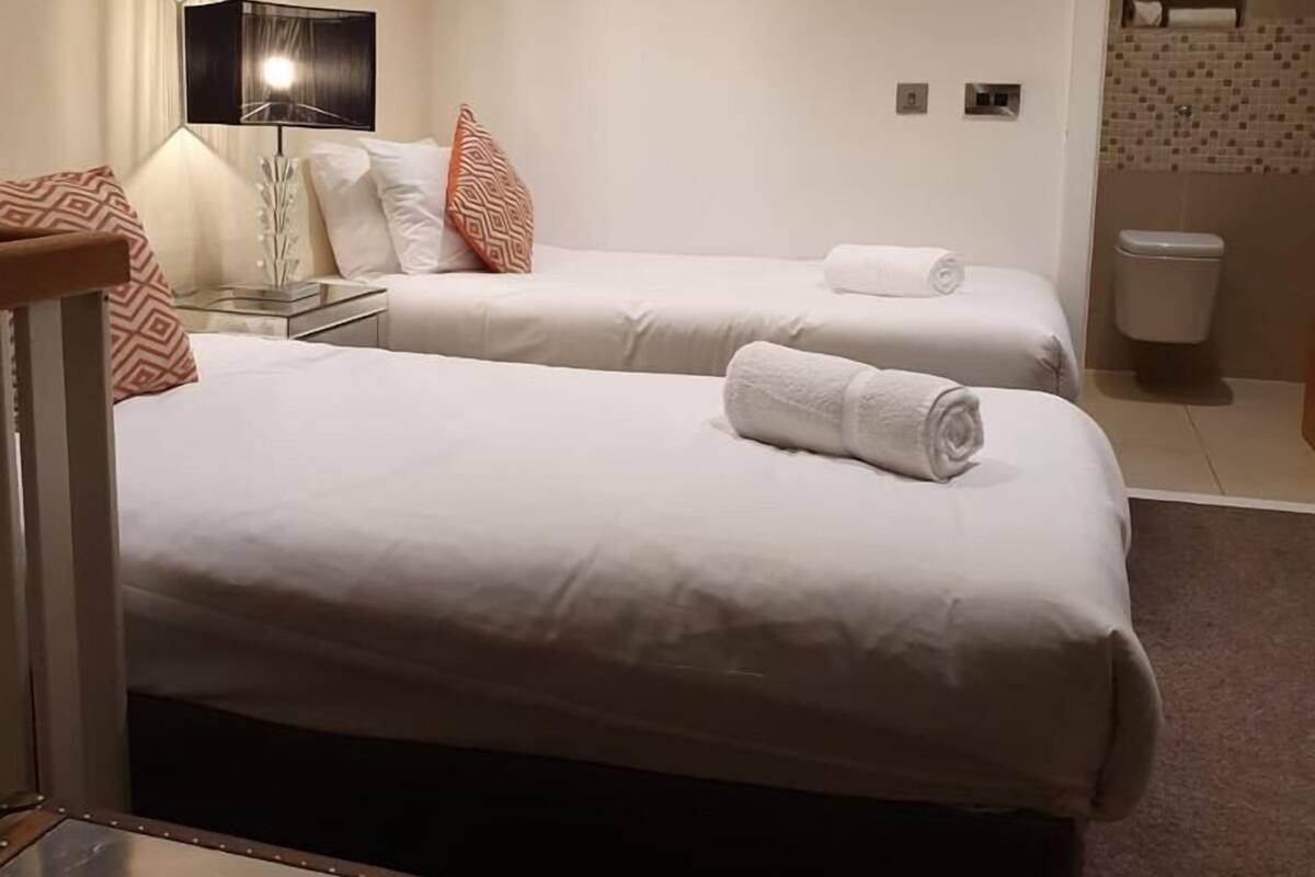 Ein Hotelzimmer mit zwei Betten, einem Schreibtisch, einer Lampe und einem durchgegangenen Tür erkennbaren Badezimmer.