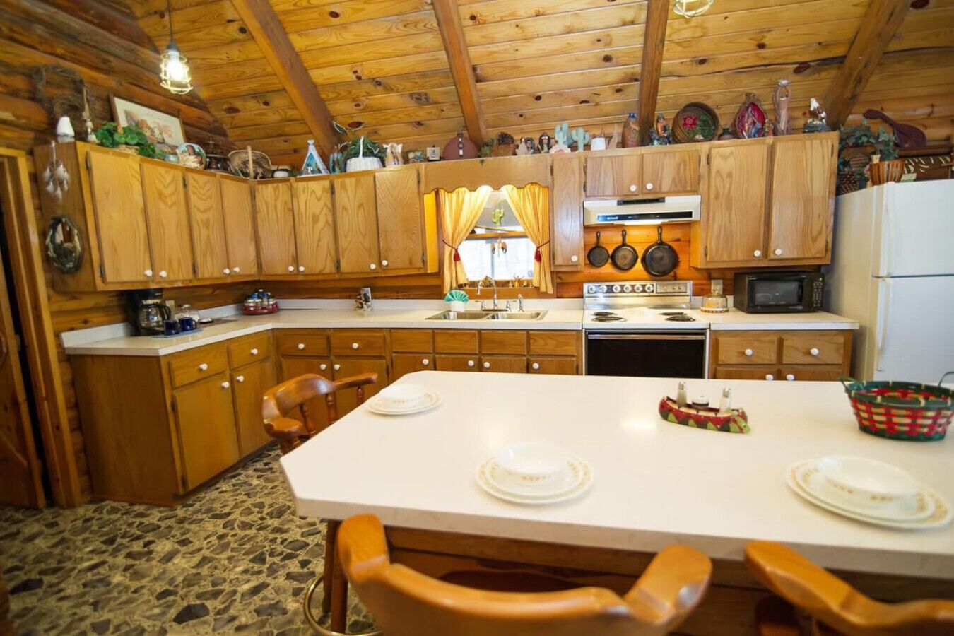 A wooden cabin kitchen with a large island, wooden cabinets, a stove, and a microwave.