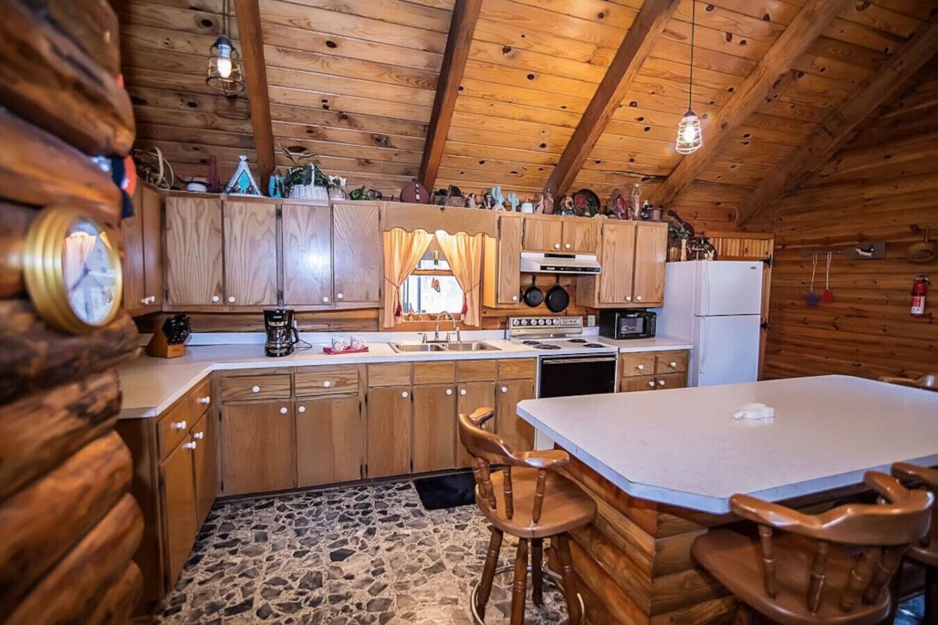 A rustic wooden cabin interior with a kitchen featuring wooden cabinets, a stone floor, and a dining area with wooden chairs.