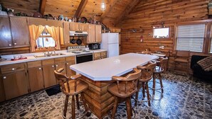 Una cabaña de madera con cocina que cuenta con una isla grande, taburetes de bar y piso de piedra.