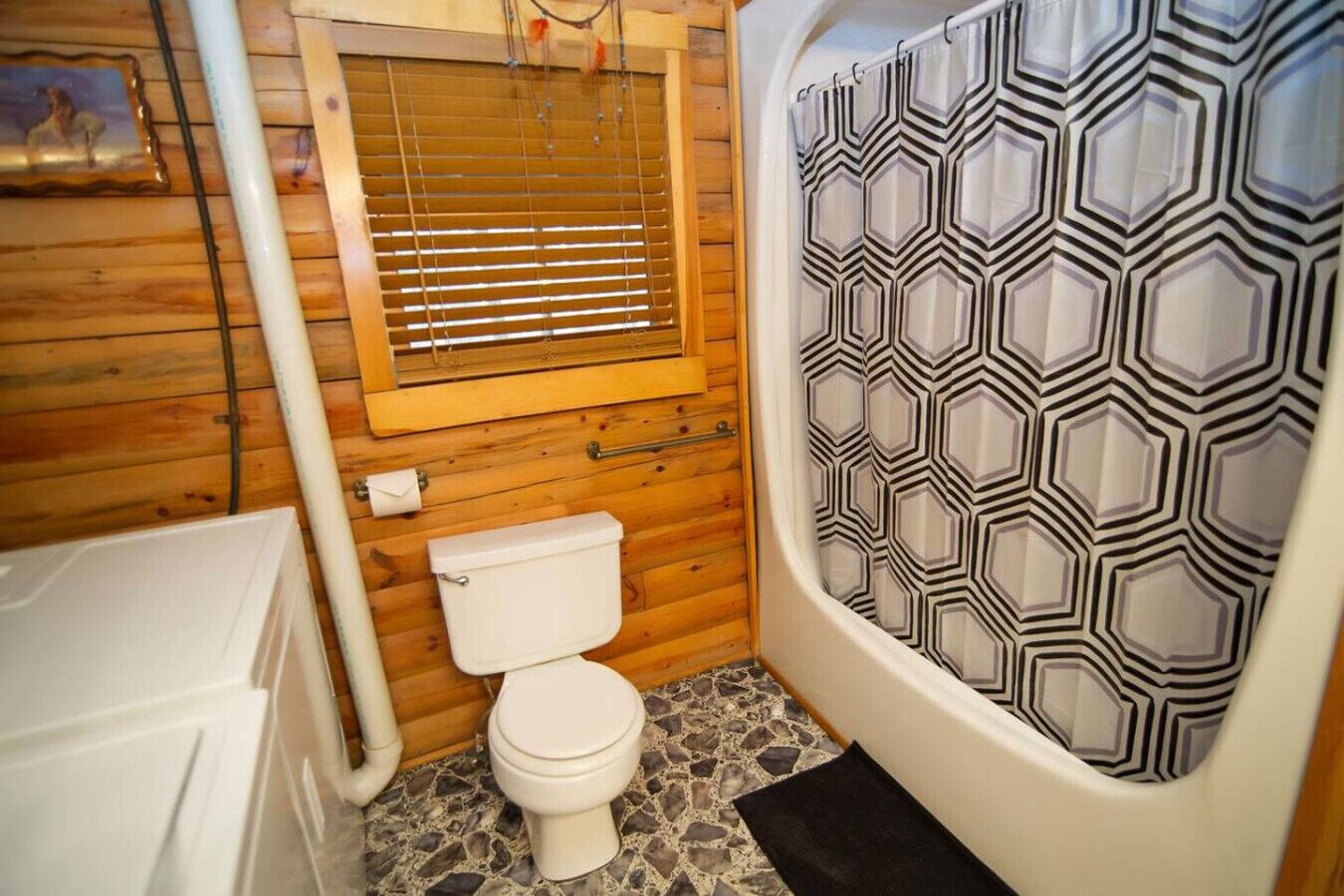 A compact bathroom with a toilet, a shower with a geometric-patterned curtain, and wooden walls.