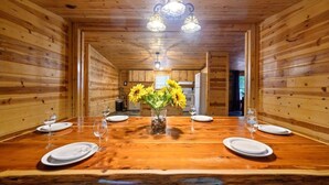 Een houten eetkamer met een lange tafel gedekt voor zes personen, een kroonluchter en een vaas zonnebloemen.