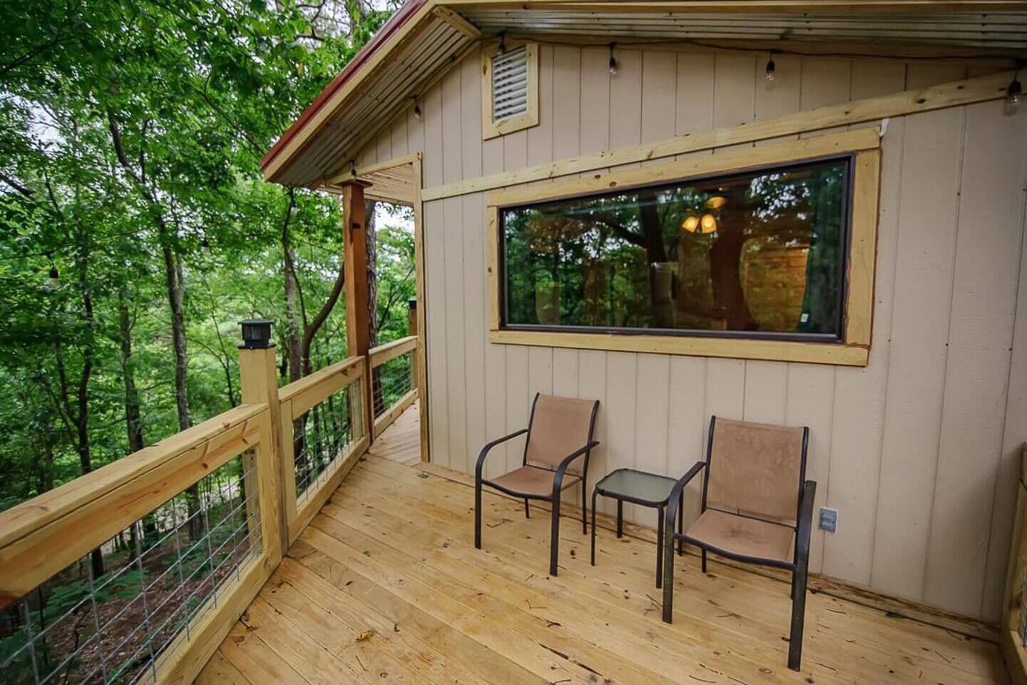 A wooden deck with two chairs and a large window overlooking a forested area.