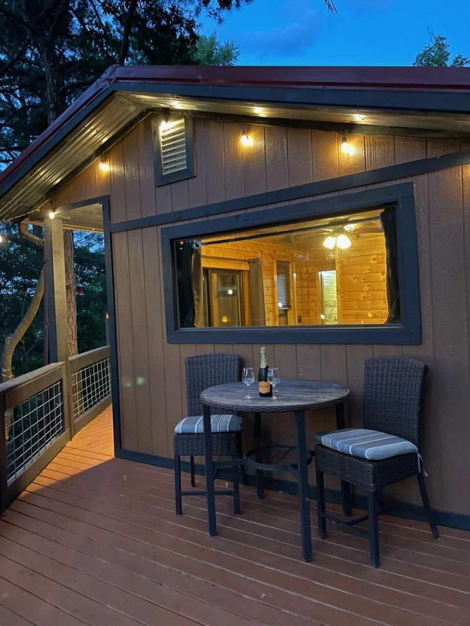 A wooden cabin with a deck, a table with chairs, and a bottle of champagne.