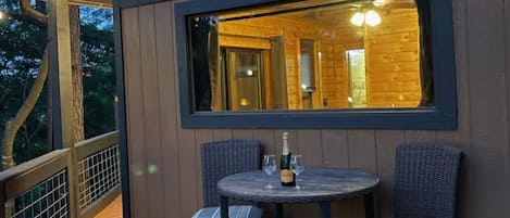 Een houten chalet met een terras, een tafel met stoelen en een fles champagne.