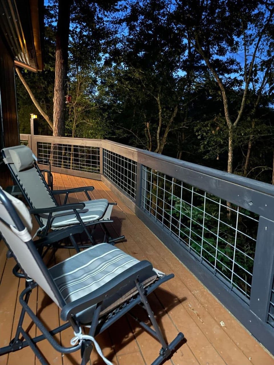 A wooden deck with two lounge chairs and a metal railing.