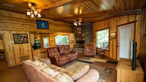 A cozy cabin interior with a stone fireplace, leather sofas, and a television.