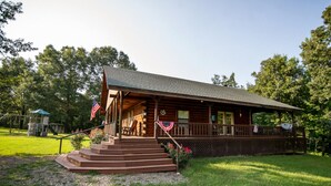 A log cabin with a porch, steps, and American flags.