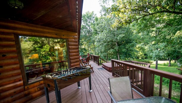 A wooden deck with a foosball table, chairs, and a glass table.
