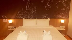 A hotel room with a large bed, two pillows, two bedside tables with lamps, and a wall mural of bamboo and birds.
