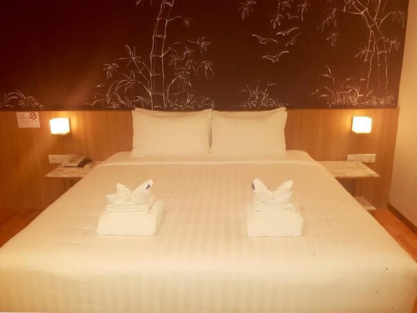 Habitación de hotel con una cama grande, dos almohadas, dos mesitas de noche con lámparas y un mural de bambú y pájaros.
