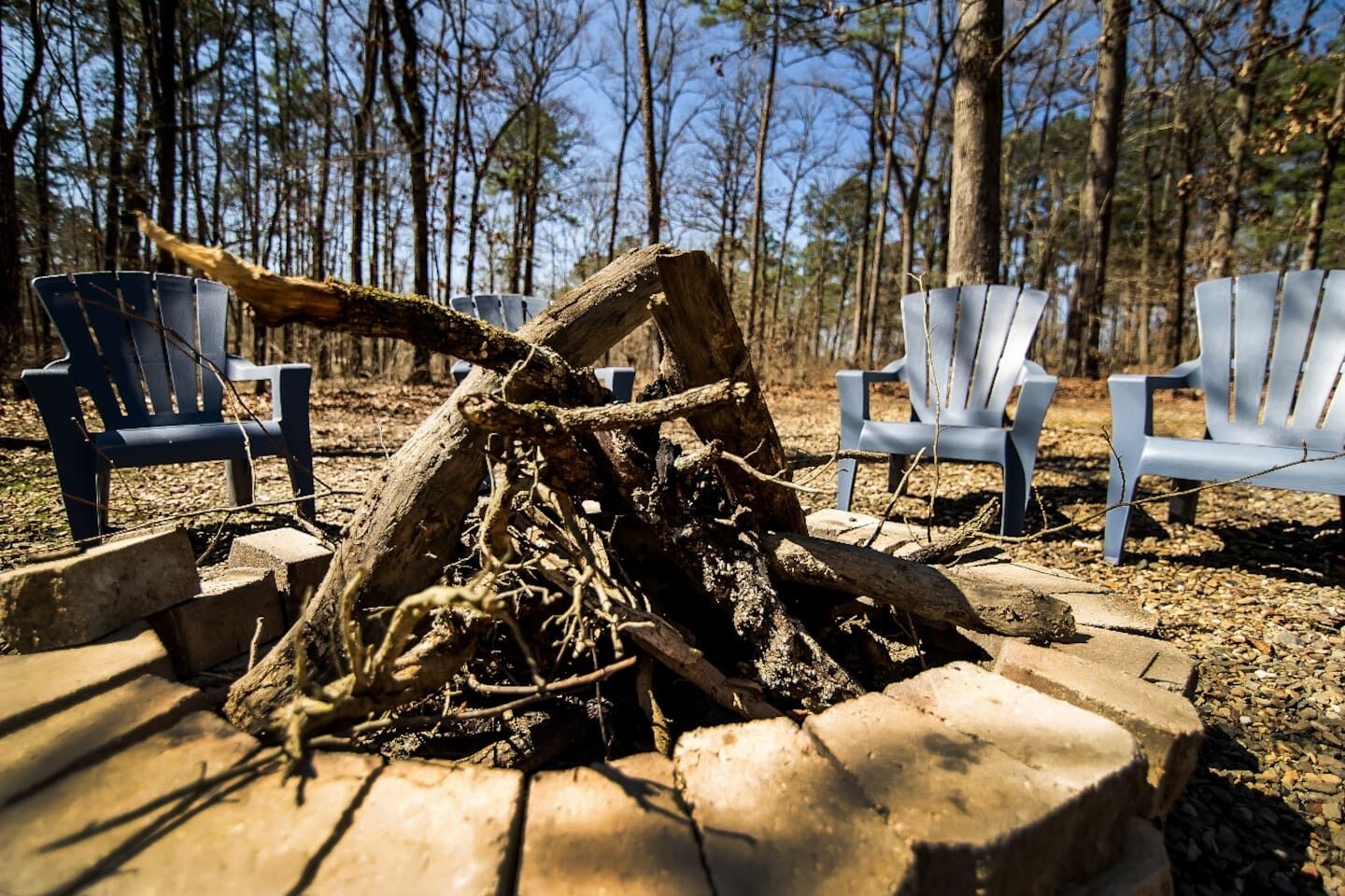 A campfire surrounded by Adirondack chairs in a forest setting.