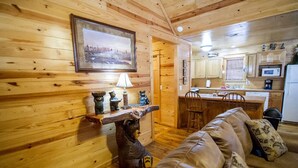 Un accogliente interno di una baita con un muro in legno, un tavolino a tema orso, un divano in pelle e un angolo cottura con mobili e elettrodomestici in legno.