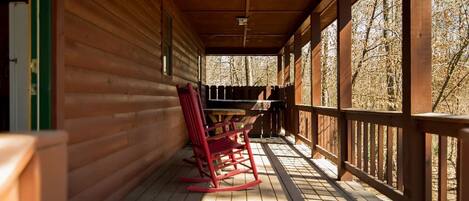 A wooden cabin with a covered porch, a rocking chair, and a table.