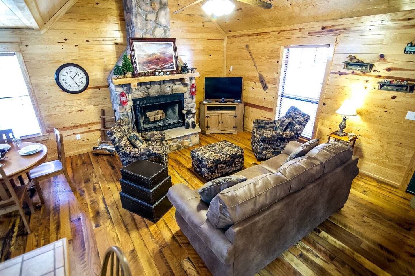 Un intérieur de chalet chaleureux avec une cheminée en pierre, des murs en bois, un coin repas et un téléviseur.