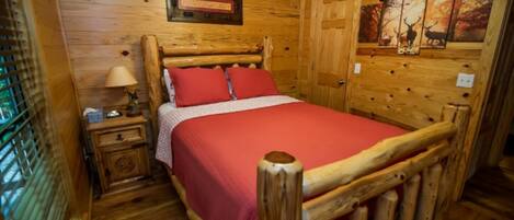 A wooden room with a bed, a nightstand, a lamp, and a framed picture on the wall.