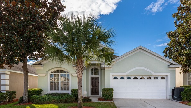 A residential house with a front garage, a palm tree, and a well-maintained lawn. - Enchanted Cottage by VillaDirect (Kissimmee)