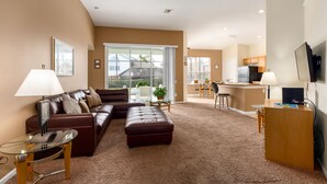 A living room with a brown leather sofa, a glass coffee table, and a television on a wooden stand. - Enchanted Cottage by VillaDirect (Kissimmee)
