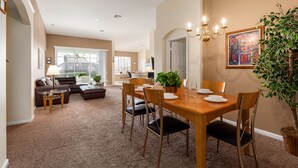 A dining area with a wooden table, chairs, and a chandelier. There is a sofa and a coffee table in the background. - Enchanted Cottage by VillaDirect (Kissimmee)
