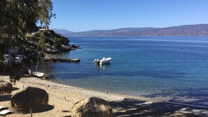 A beach with thatched umbrellas, a boat, and a clear view of the water. - Arbeli House for idyllic sun & sea holidays in Mandraki Bay, Hydra (Idra)